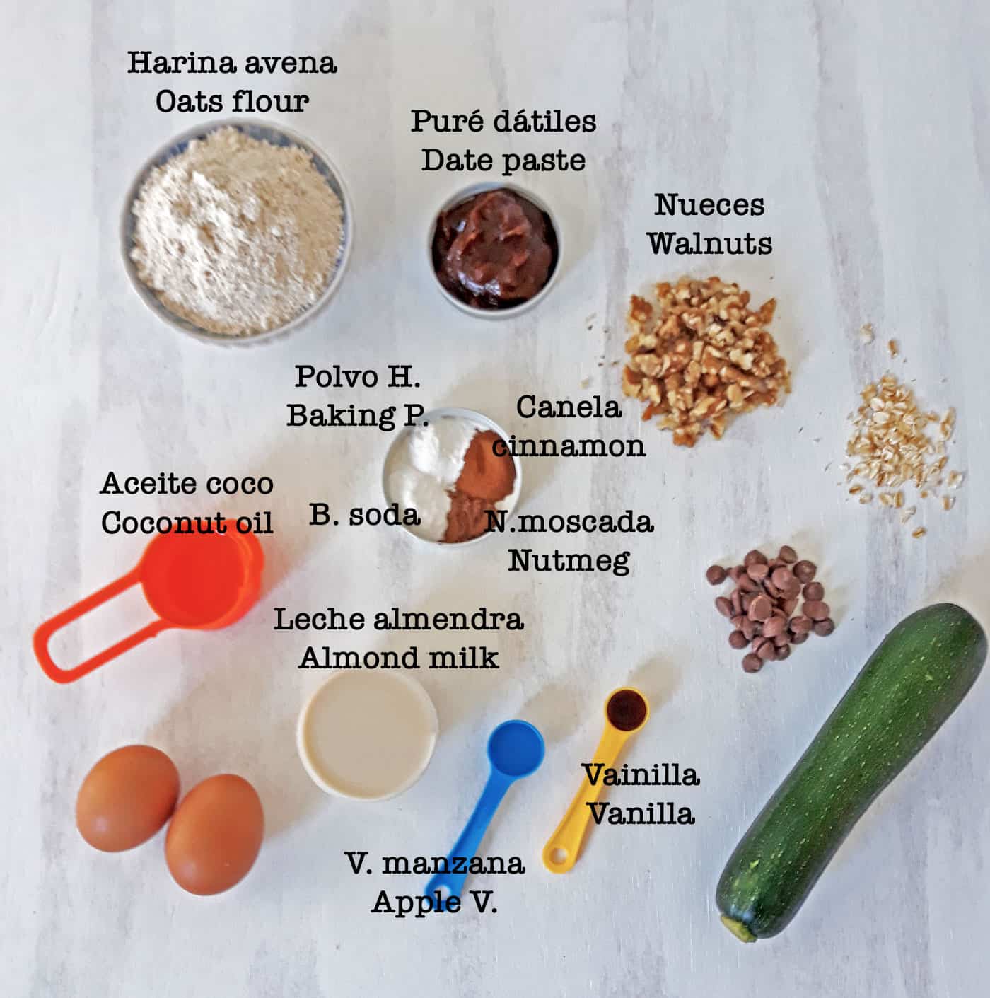 ingredientes para preparar muffins de zucchini sobre una mesa blanca