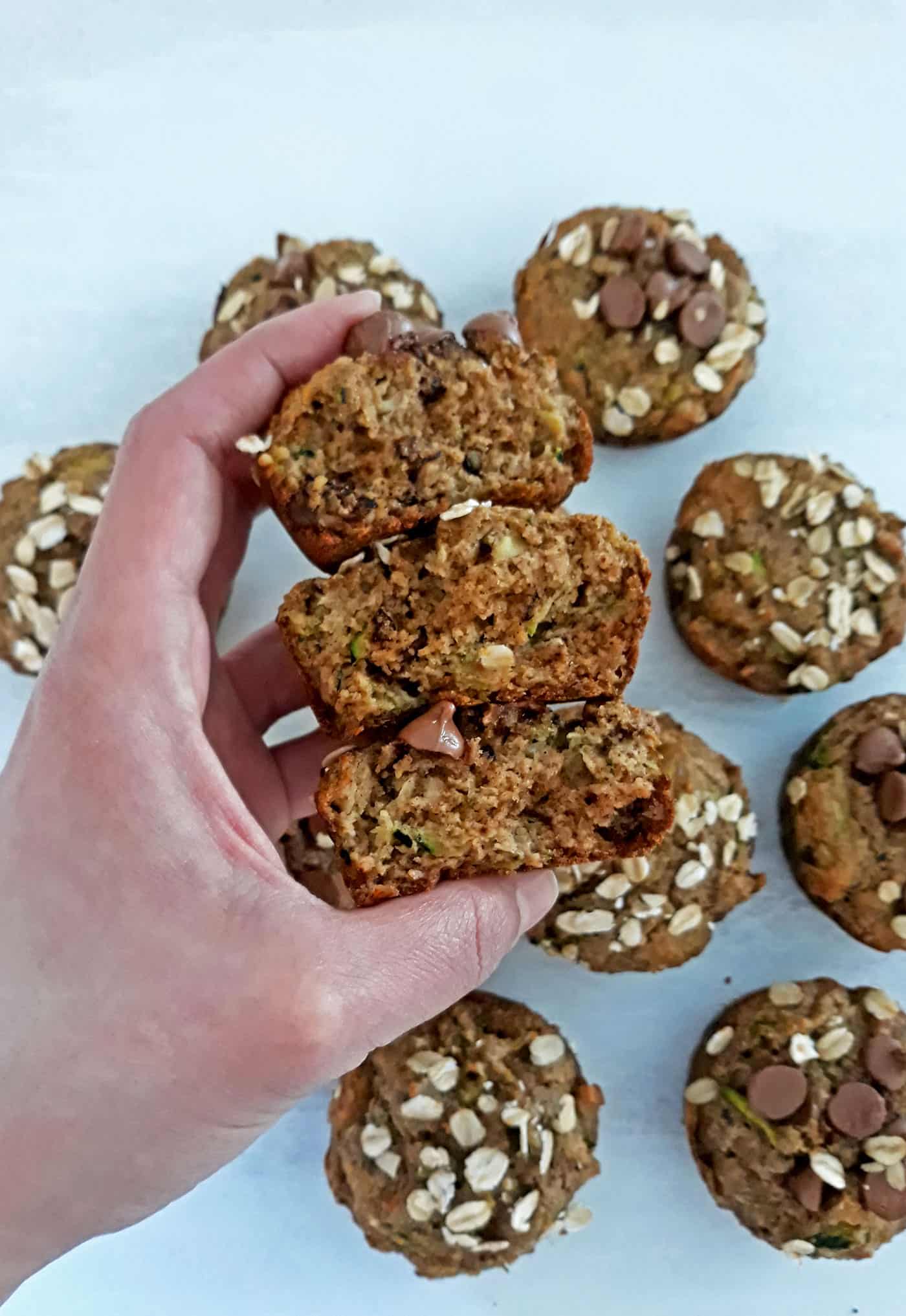 mano de una mujer sosteniendo tres muffins de Zucchini partidos por la mitad