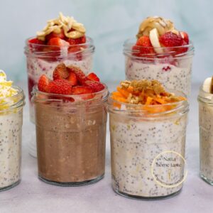Vasos de vidrio con avena trasnochada decorada con fresas, mantequilla de maní, zanahoria rallada y otros toppings, ideal para un desayuno saludable y meal prep.