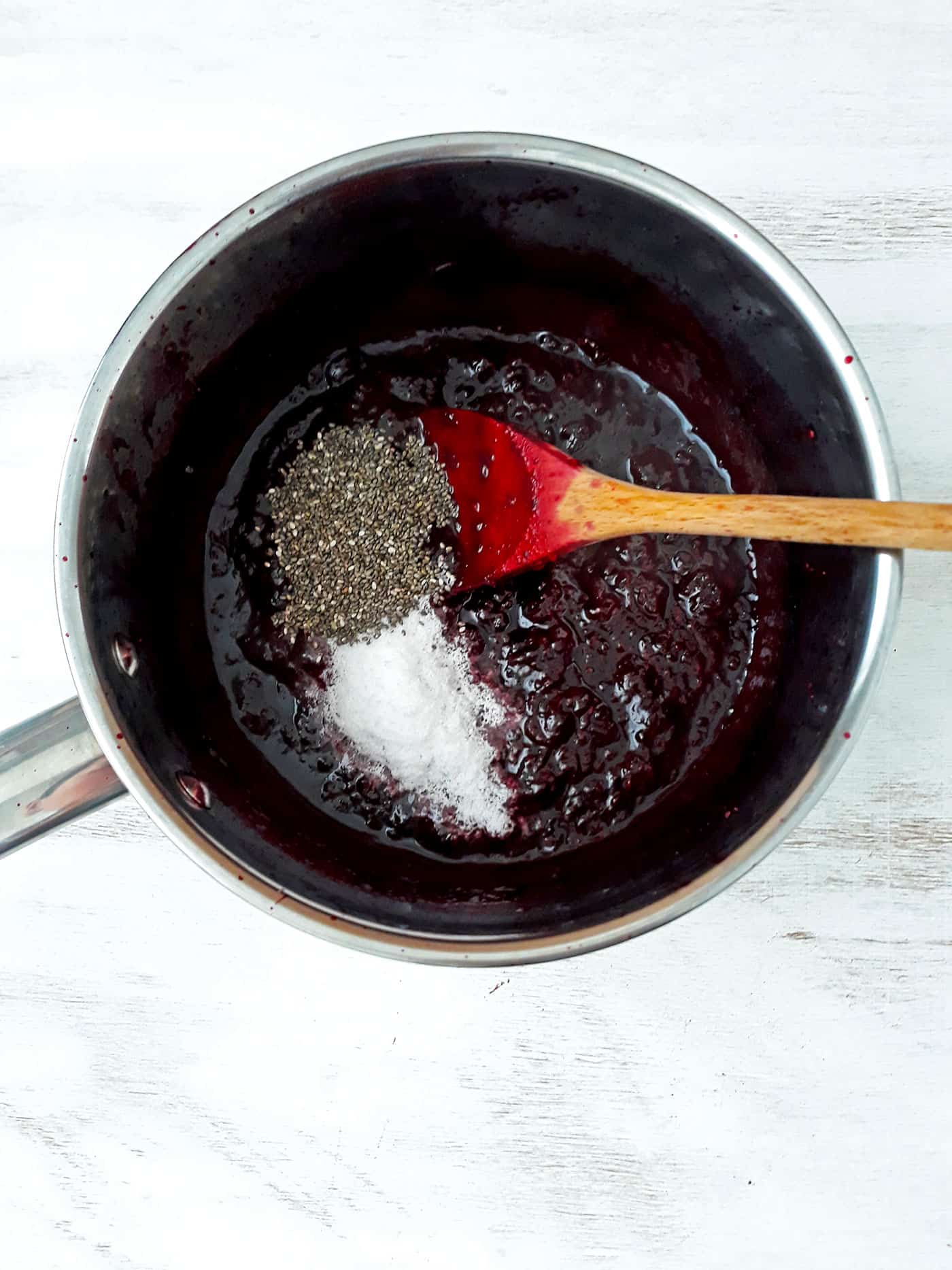 mermelada de frutos rojos en una olla con semillas de chía stevia y una cuchara de palo