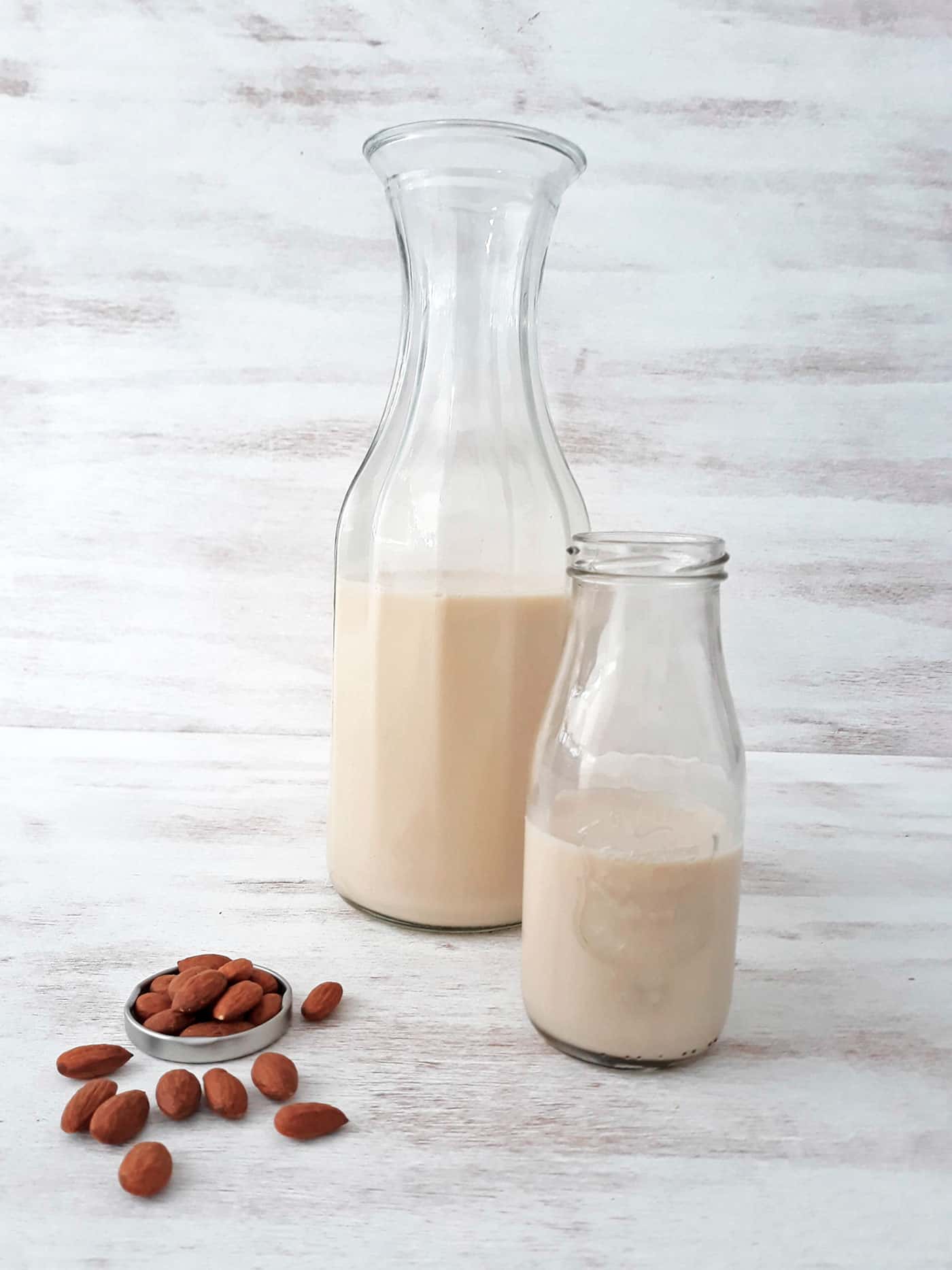 dos botellas de vidrio con leche de almendras sobre una mesa blanca