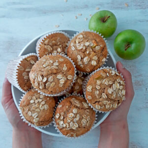 muffins de manzana en un contenedor blanco con dos manzanas frescas