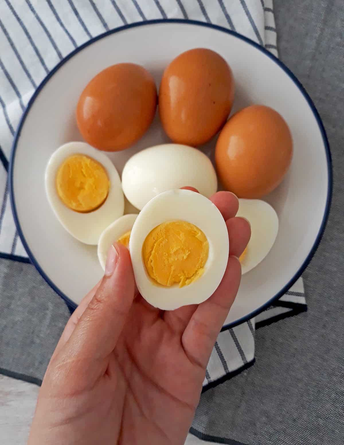huevo duro en la mano de una mujer y otros huevos con cascaras y sin cascaras servidos en un plato