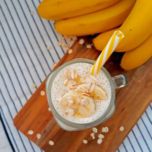 smoothie de banana con un pitillo amarillo y blanco acompañado de bananas