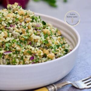 Ensalada de garbanzos mediterránea en un recipiente redondo blanco sobre una mesa con un tenedor.