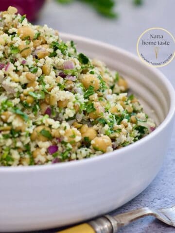 Ensalada de garbanzos mediterránea en un recipiente redondo blanco sobre una mesa con un tenedor.