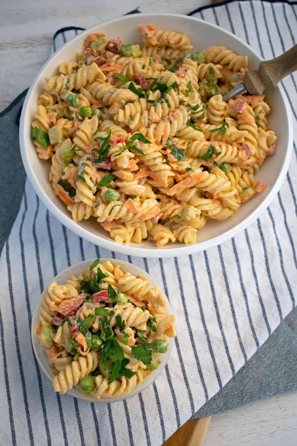 ensalada de pasta con aderezo de yogur griego servida en un plato blanco y un contenedor plástico