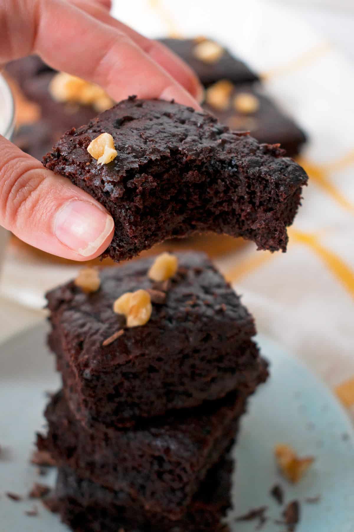 brownie mordido en la mano de una mujer, con más brownies en el fondo.