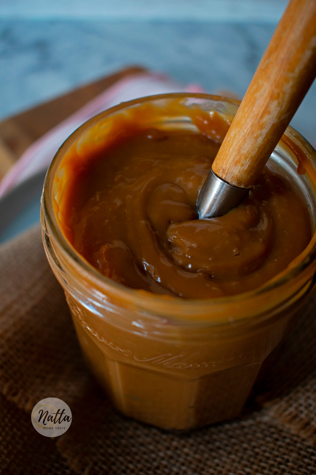 un frasco de vidrio con dulce de leche con una cuchara de madera adentro.