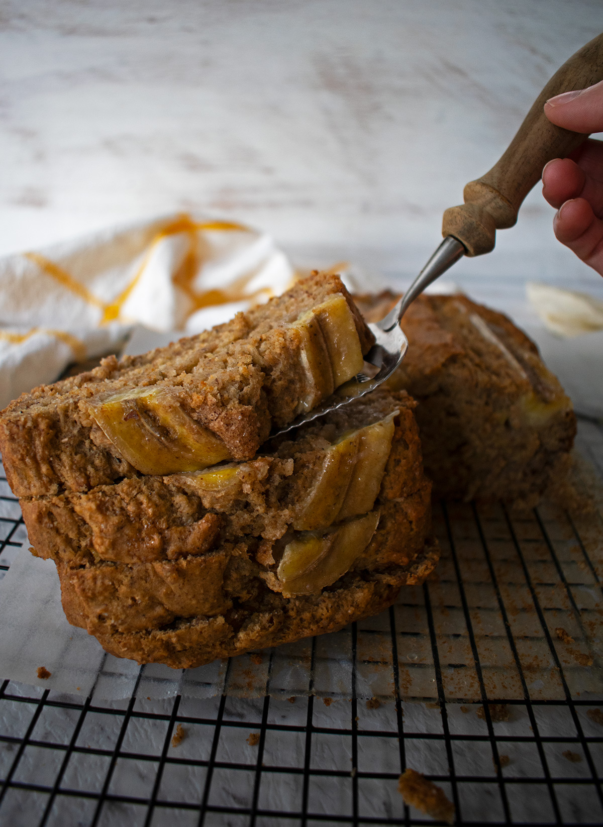 Porciones de pan de banana sobre una rejilla, una de las porciones la están tomando con una espátula.