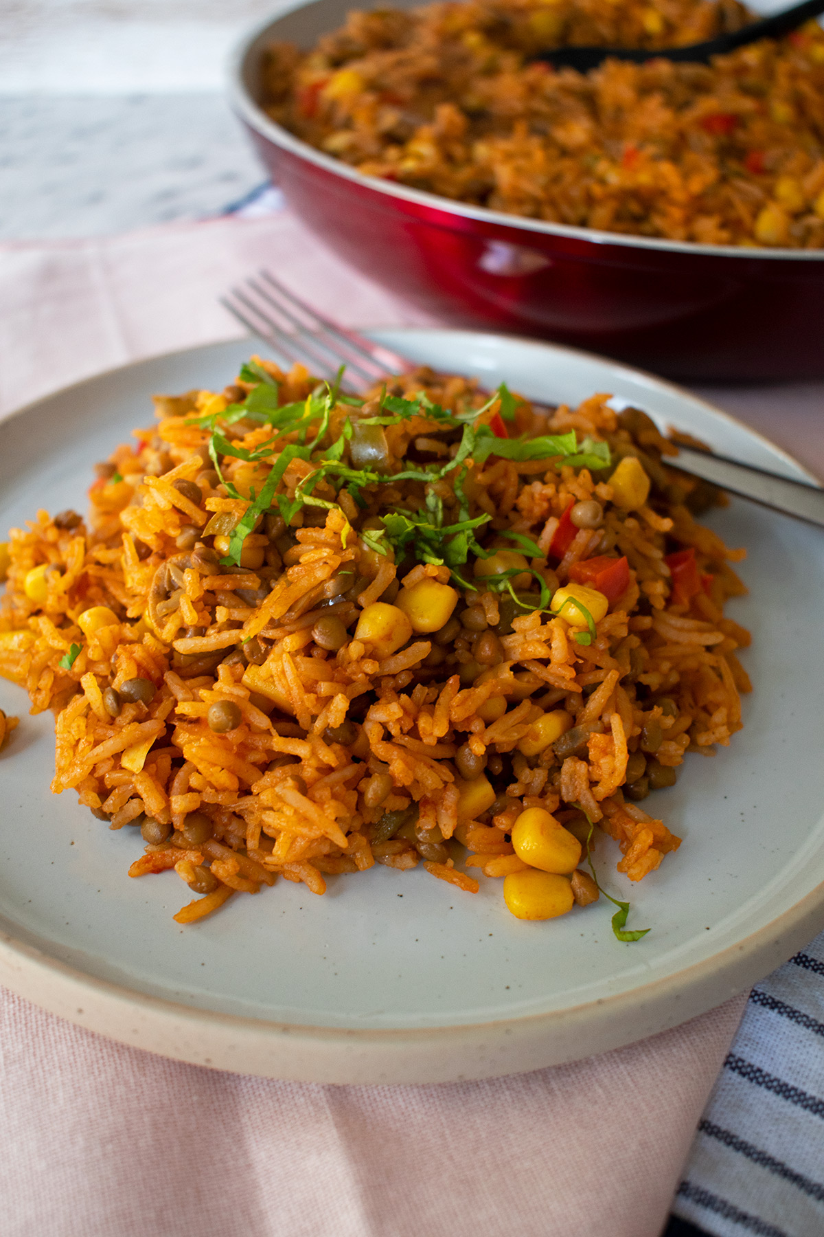 Arroz con verduras servido en un plato redondo con un sartén al fondo.