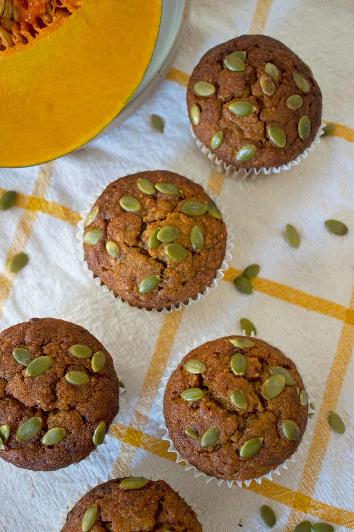 muffins de zapallo sobre un paño blanco con lineas amarillas, acompañados de media calabaza.