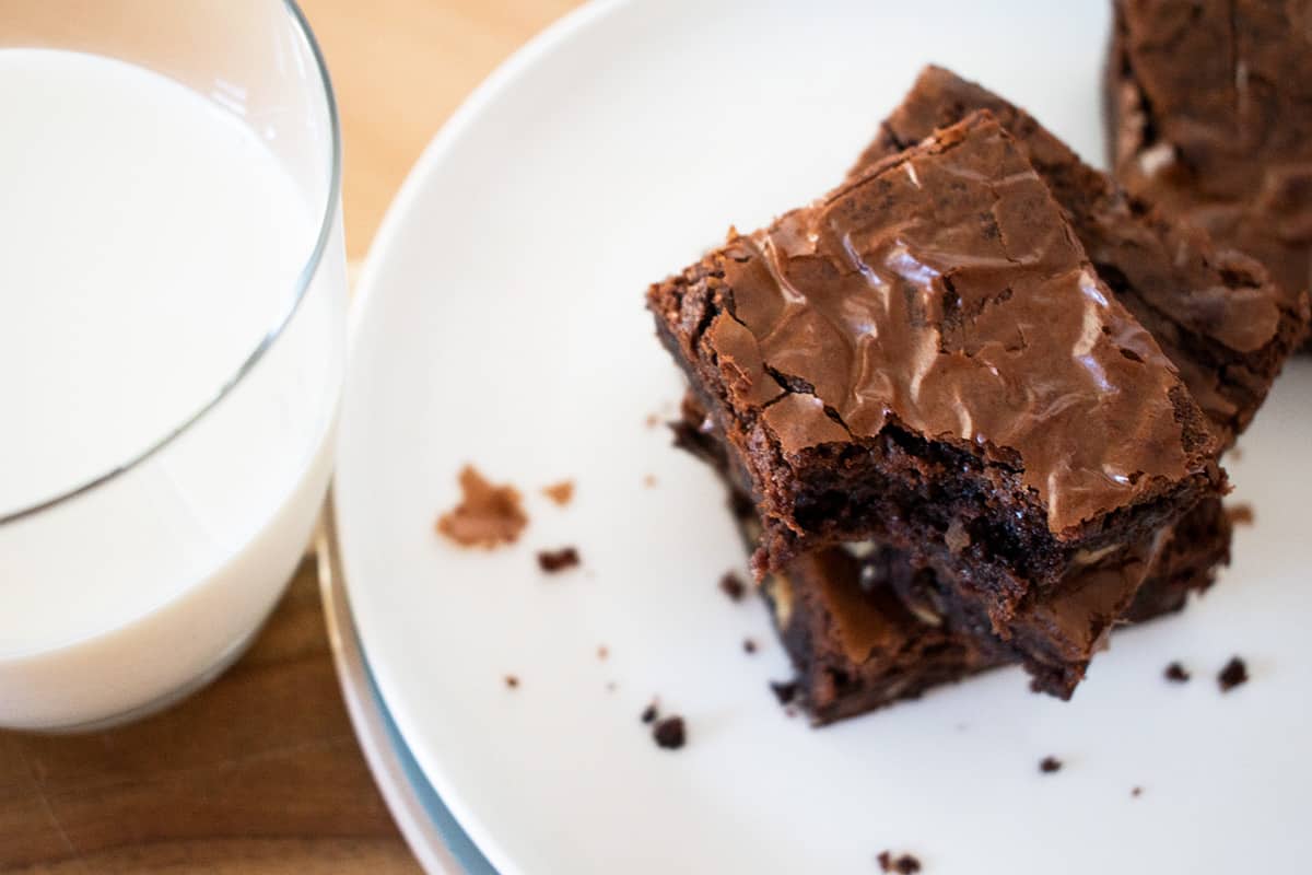 brownies de chocolate servidos en un plato blanco acompañados de un vaso de leche.