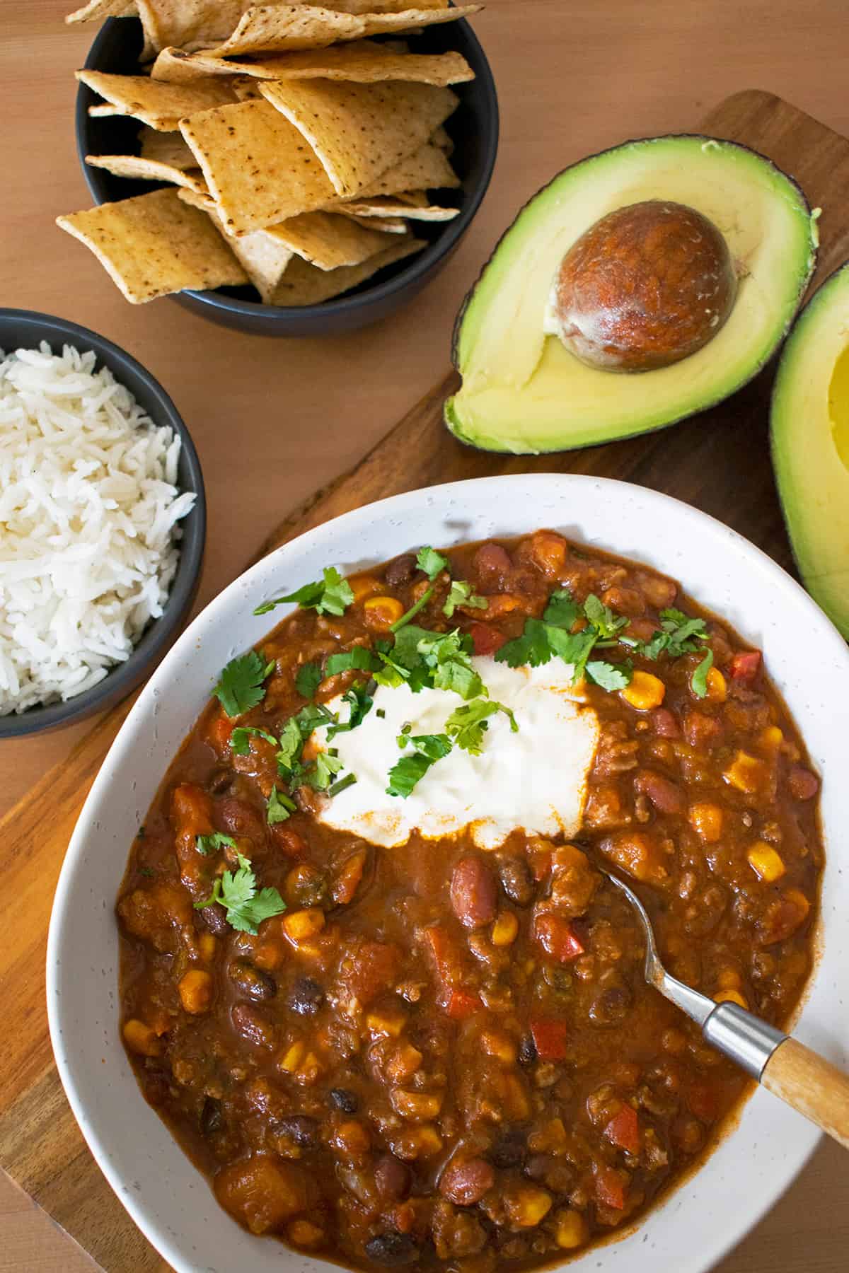 chili con carne acompañado de arroz, chips de maíz y aguacate.