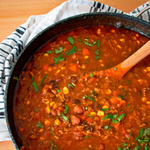 chili con carne en una olla grande con una cuchara de madera