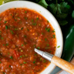 salsa fresca estilo mexicano servida en un plato redondo blanco con una cuchara de madera