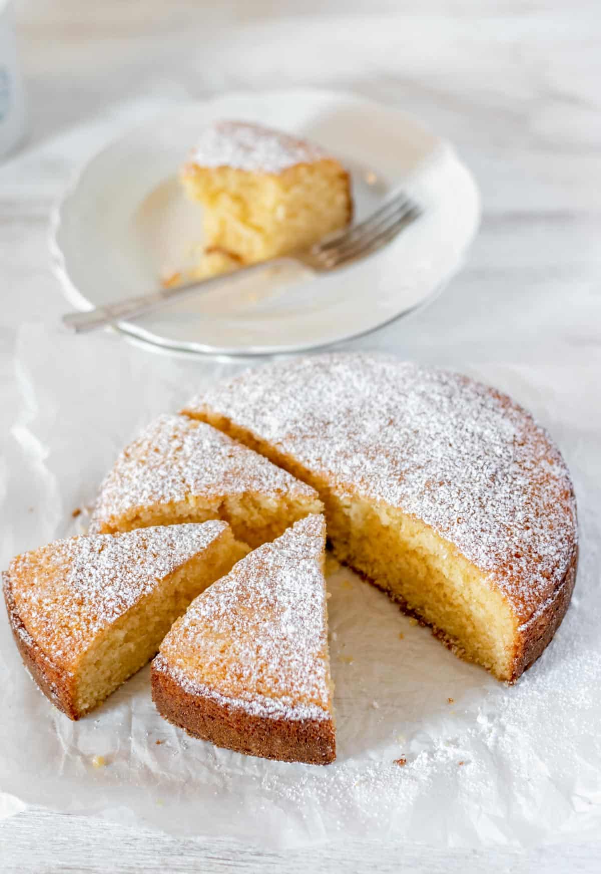 Pastel de vainilla casero redondo partido en porciones triangulares sobre una mesa blanca.