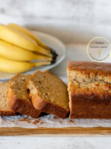 Pan de banana partido en rebanadas servido sobre una tabla de madera acompañado de bananos frescos