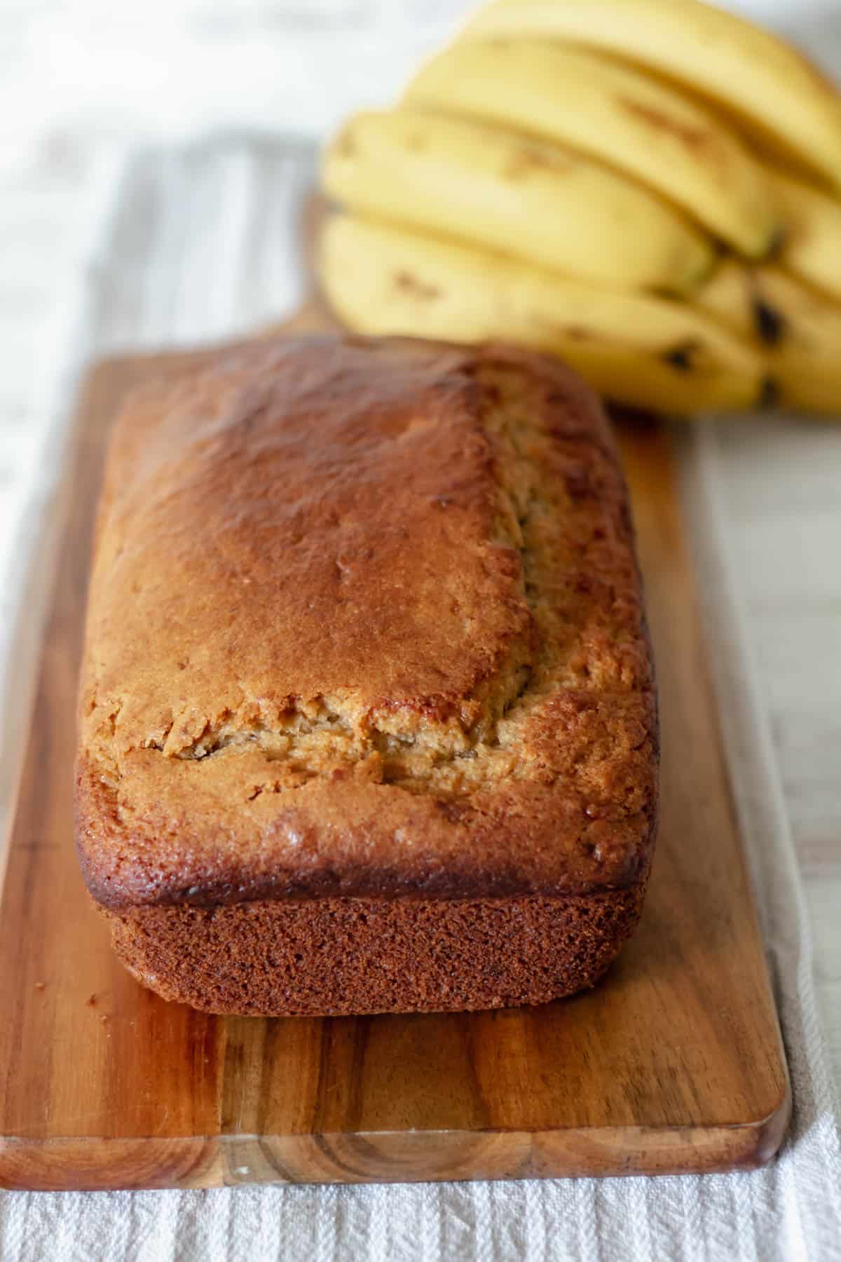 pan de plátano servido sobre una tabla de madera con bananos frescos en la parte de atrás.