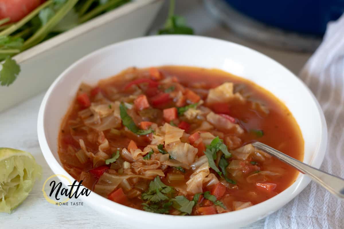 Sopa de repollo servida en un plato blanco con una cuchara plateada