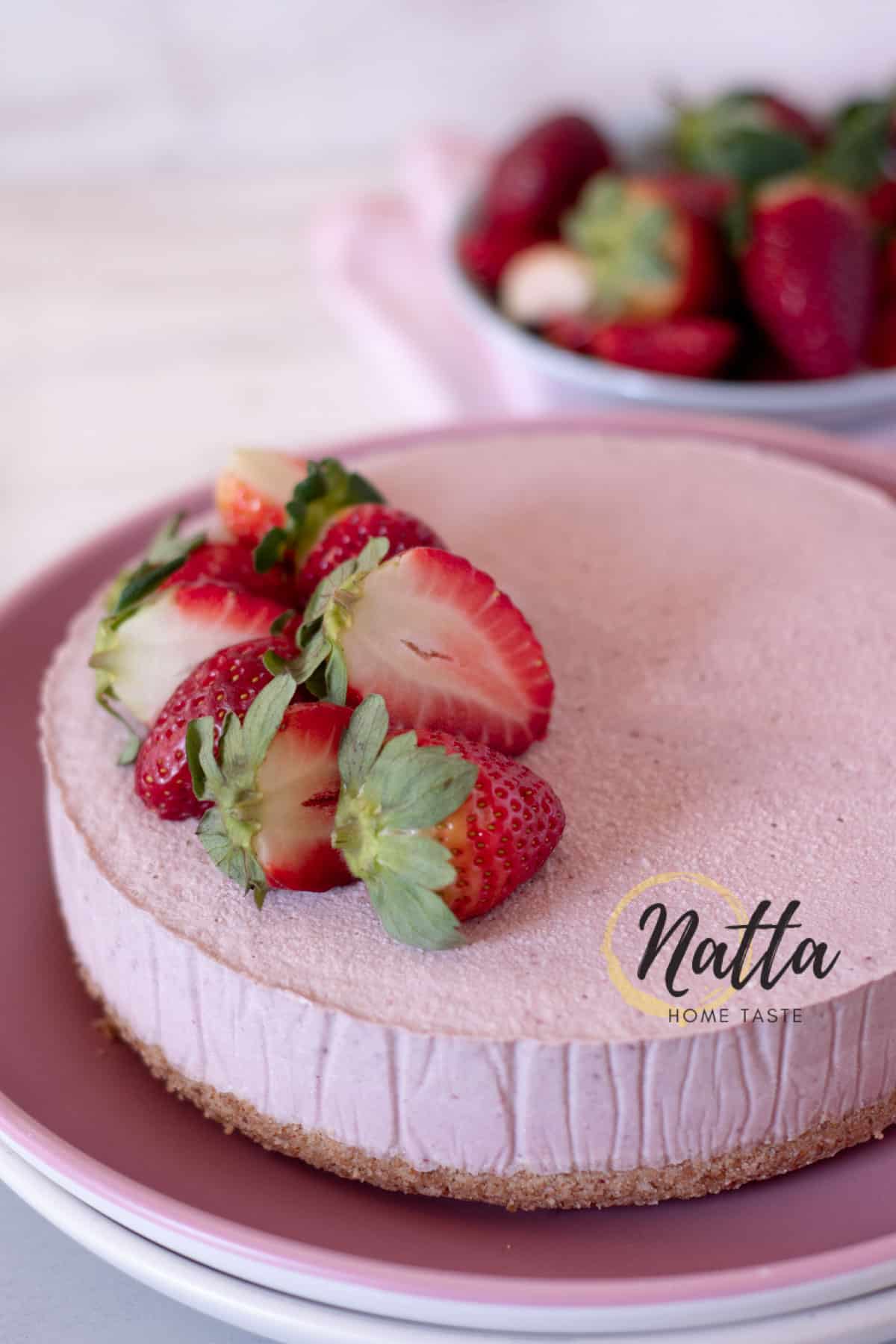 Cheesecake vegano de fresa servido en un plato rosado.