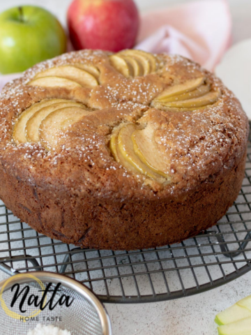 torta de manzana sobre una mesa blanca con 2 manzanas atrás