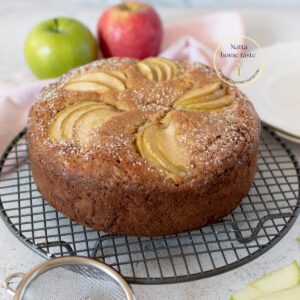 torta de manzana sobre una mesa blanca con 2 manzanas atrás