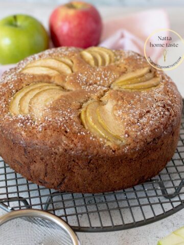 torta de manzana sobre una mesa blanca con 2 manzanas atrás