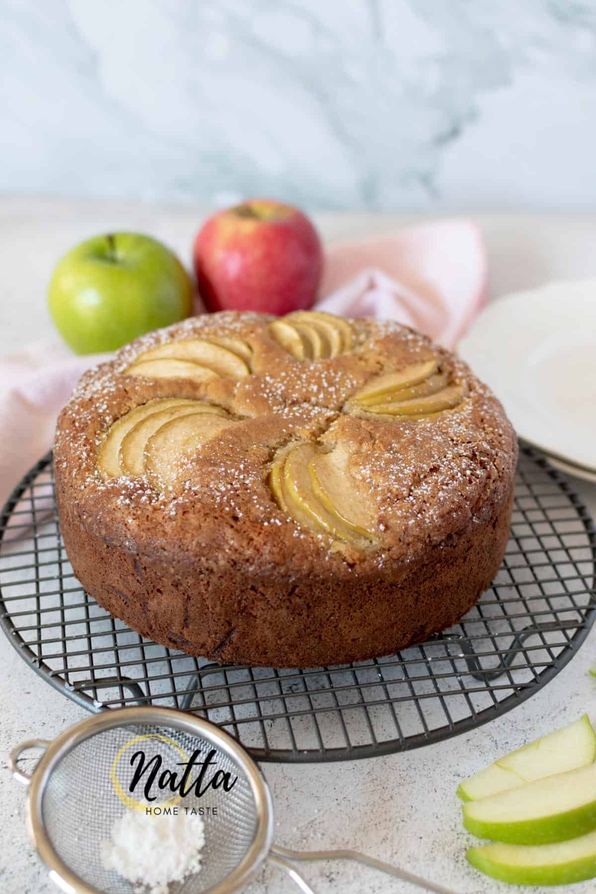 torta de manzana servida sobre una parrilla acompañada de una manzana roja y verde