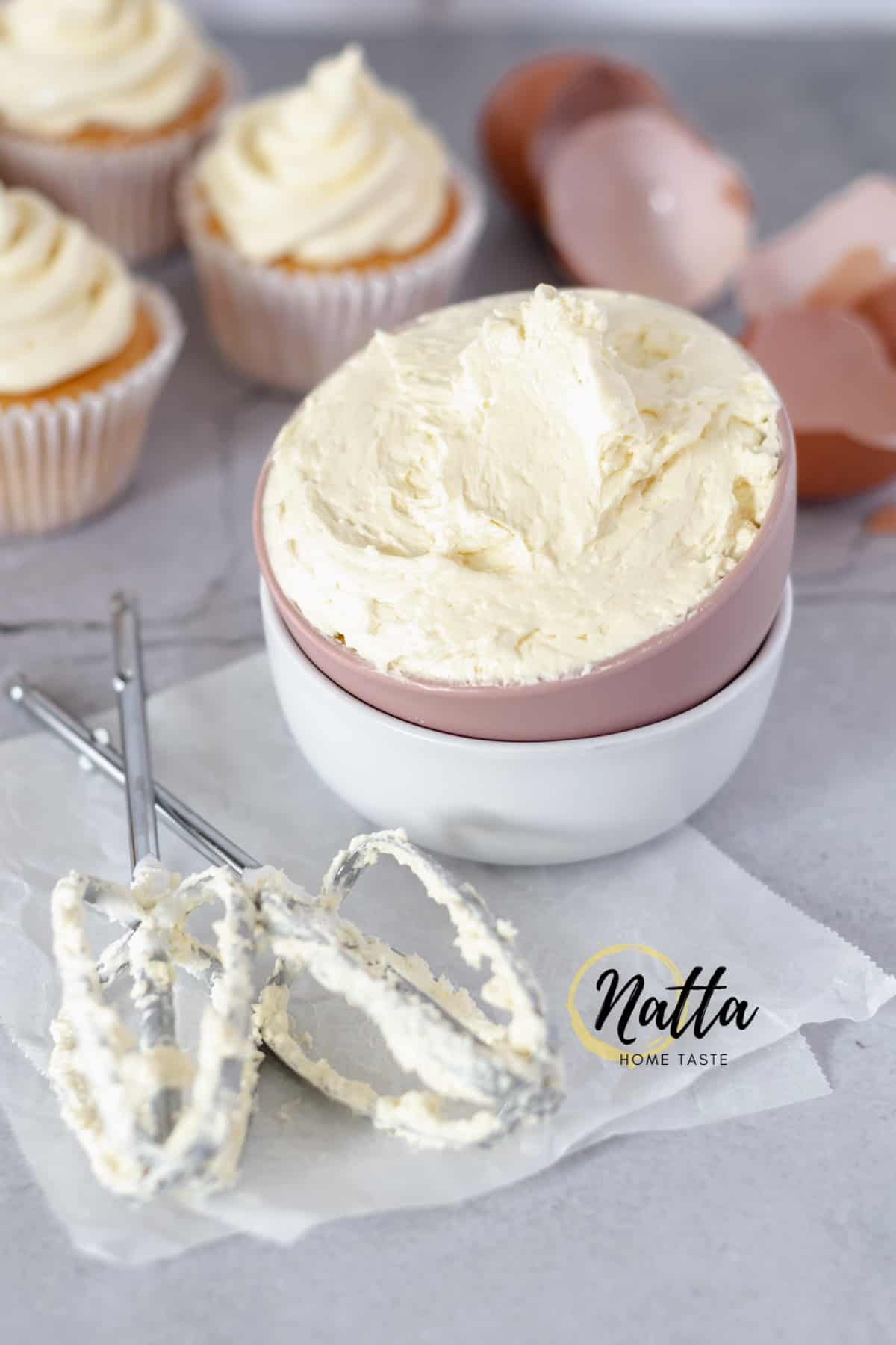 taza de crema de mantequilla de merengue suizo con cupacakes de vainilla en la parte de atrás.