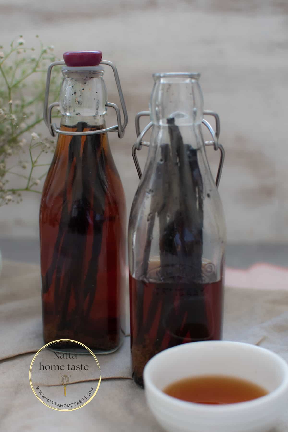 dos botellas de vidrio con extracto de vainilla casero con un pequeño contenedor blanco al lado.