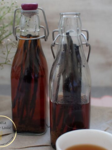 dos botellas de vidrio con extracto de vainilla casero con un pequeño contenedor blanco al lado.