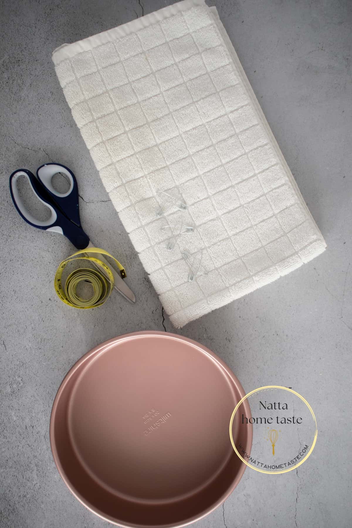 Materiales para hacer bandas o tiras caseras para hornear bizcochos planos. Una toalla blanca, ganchos, tijeras, un molde rosado redondo.