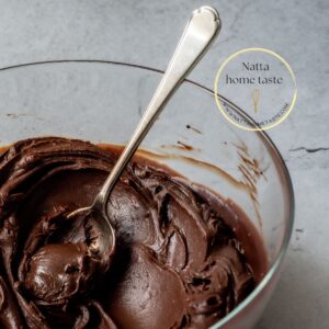 Ganache de chocolate para cobertura servido en un bol transparente con una cuchara plateada sobre una mesa gris.