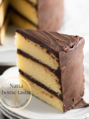 porción de torta de vainilla cubierta de ganache de chocolate servida en un plato blanco.