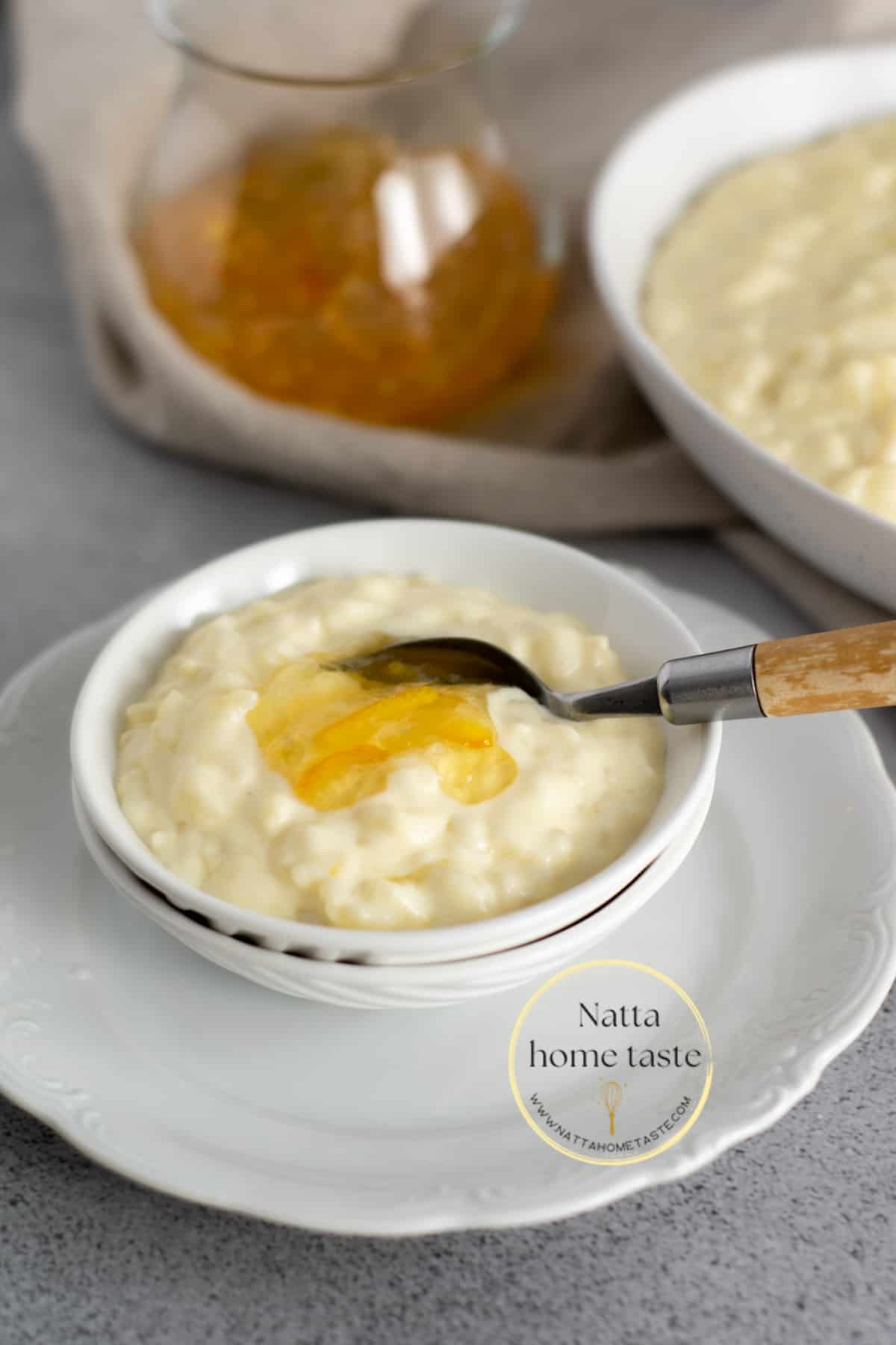 Arroz con leche servido un pequeño bol blanco sobre un plato redondo también blanco servido con una cuchara con mango de madera.