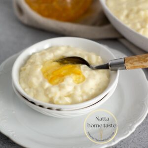 Arroz con leche servido en un pequeño bol blanco sobre un plato redondo también blanco con una cuchara con mango de madera