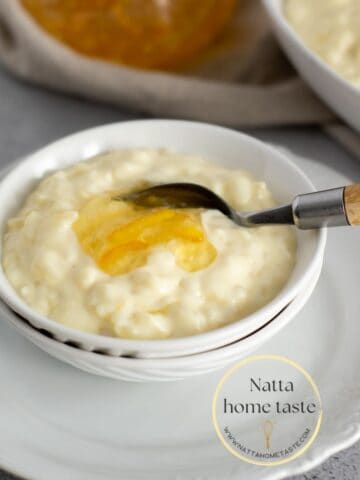 Arroz con leche servido en un pequeño bol blanco sobre un plato redondo también blanco con una cuchara con mango de madera