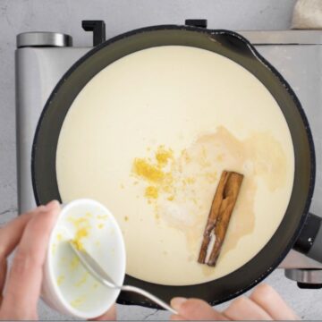 leche, astilla de canela y ralladura de limón en una olla mediana negra sobre un quemador eléctrico.