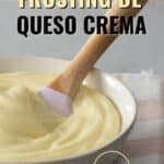 Glaseado de queso crema servido en un bol color crema con una espátula de silicona con mango de madera. el bol esta sobre una servilleta de tela con cuadros rosados y blancos.
