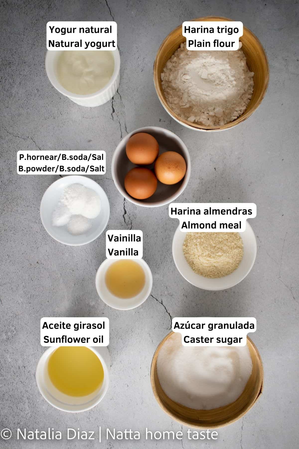 Ingredientes para preparar un bizcocho de yogur. Yogur natural, harina de trigo, huevos, polvo de hornear, bicarbonato de soda, harina de almendras, extracto de vainilla, aceite de girasol, azúcar granulada. todos los ingredientes servidos en contenedores separados.