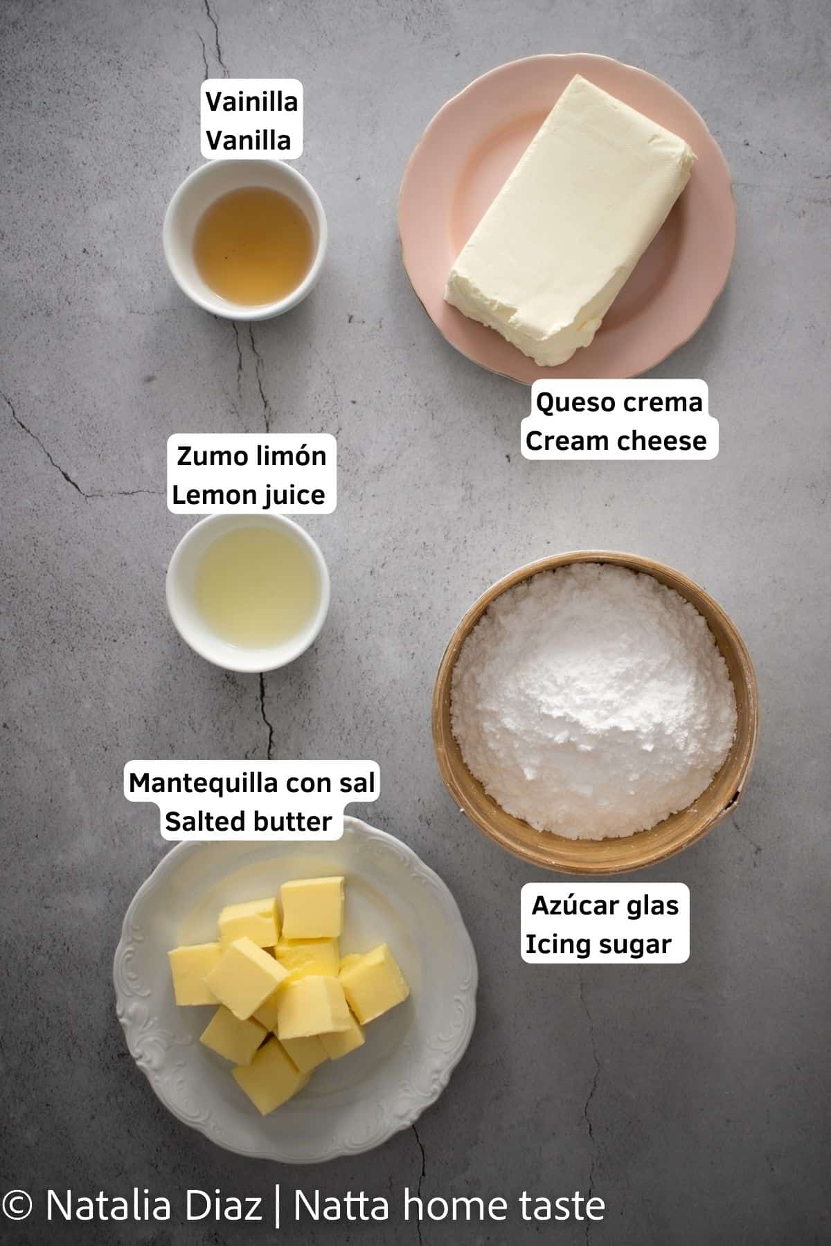 Ingredientes para preparar frosting de queso crema. queso crema en barra servido en un plato redondo rosado, azúcar glas servido en un bol redondo de madera, mantequilla partida en cuadros en un plato redondo blanco. extracto de vainilla y zumo de limón servidos en pequeños contenedores.