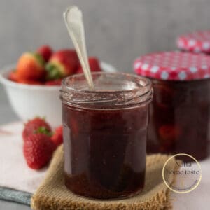 frasco de vidrio con mermelada de fresa casera y una cuchara dentro del frasco. Fresas frescas en la parte de atrás.