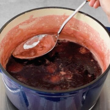 mermelada de fresa en una olla. una cuchara metálica sacando la espuma blanca que se forma durante la cocción de la mermelada.