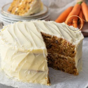 Torta de zanahoria casera de dos capas con frosting de queso crema. Zanahorias pequeñas en la parte de atrás con una porción de pastel servida sobre unos platos pequeños.