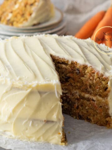 Torta de zanahoria casera de dos capas con frosting de queso crema. Zanahorias pequeñas en la parte de atrás con una porción de pastel servida sobre unos platos pequeños.