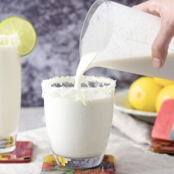 alguien vertiendo limonada de coco a un vaso de cristal corto.