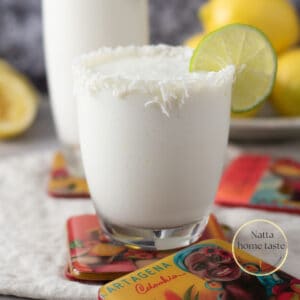 Toma frontal de dos vasos de cristal con limonada de coco servidos con rodajas de limón sobre porta vasos de Cartagena de Indias.