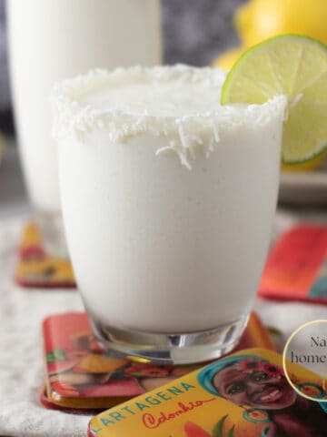 Toma frontal de dos vasos de cristal con limonada de coco servidos con rodajas de limón sobre porta vasos de Cartagena de Indias.