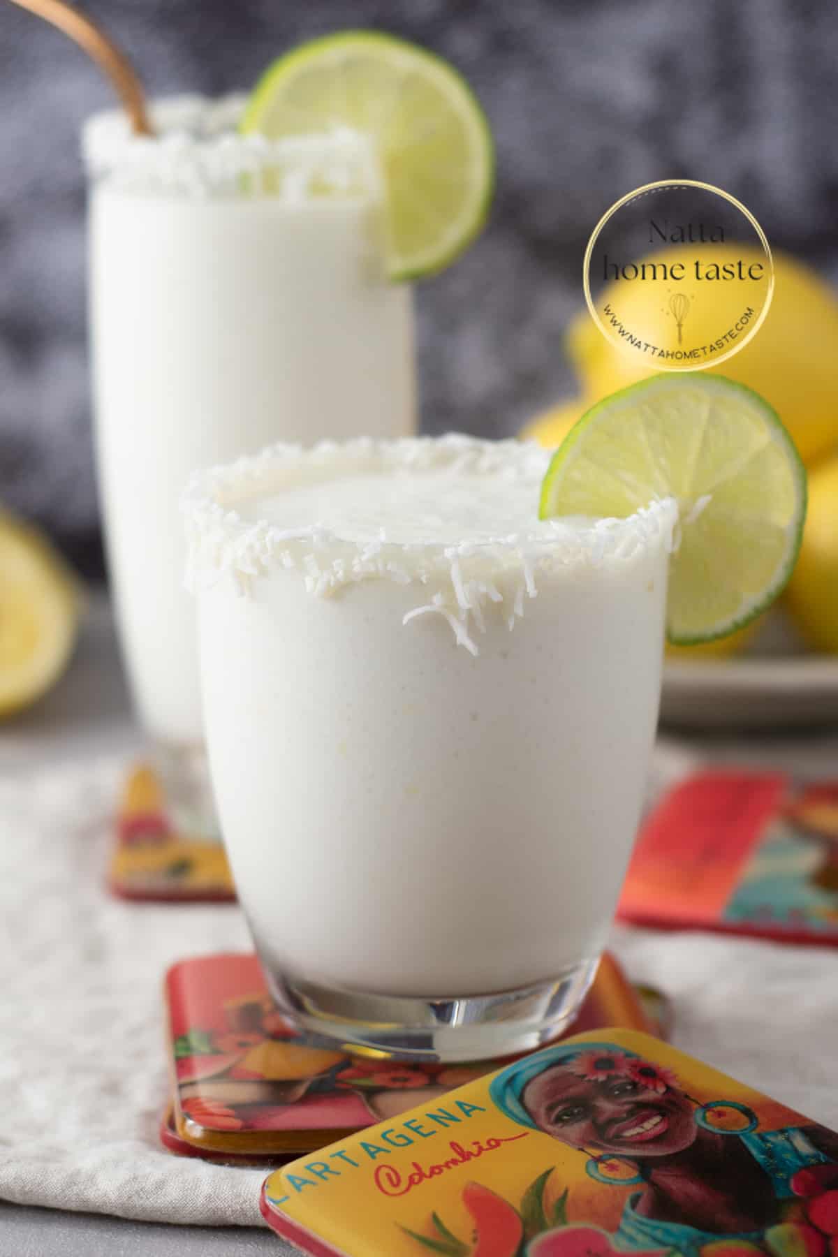 Toma frontal de dos vasos de cristal con limonada de coco servidos con rodajas de limón sobre porta vasos de Cartagena de Indias.